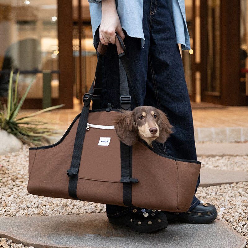 Extra-long dog carrier carried by hand outdoors, giving a small Dachshund a comfortable ride on daily walks.
