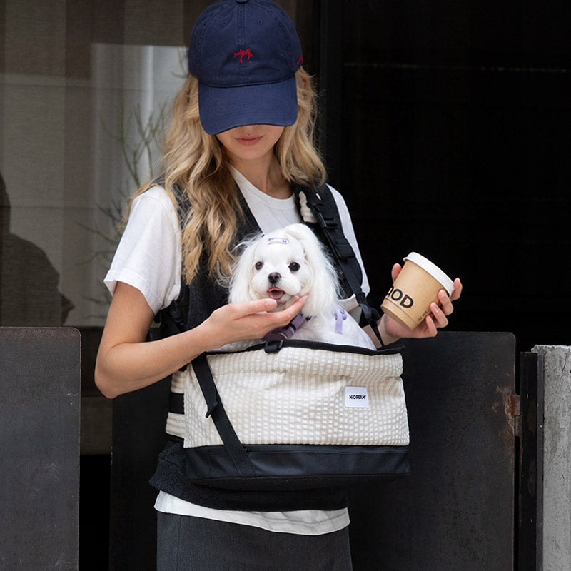 Crossbody dog carrier in vanilla beige keeps a white Maltese close during relaxed coffee runs and city errands.